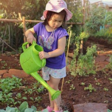 Girl watering plants with watering can in the garden